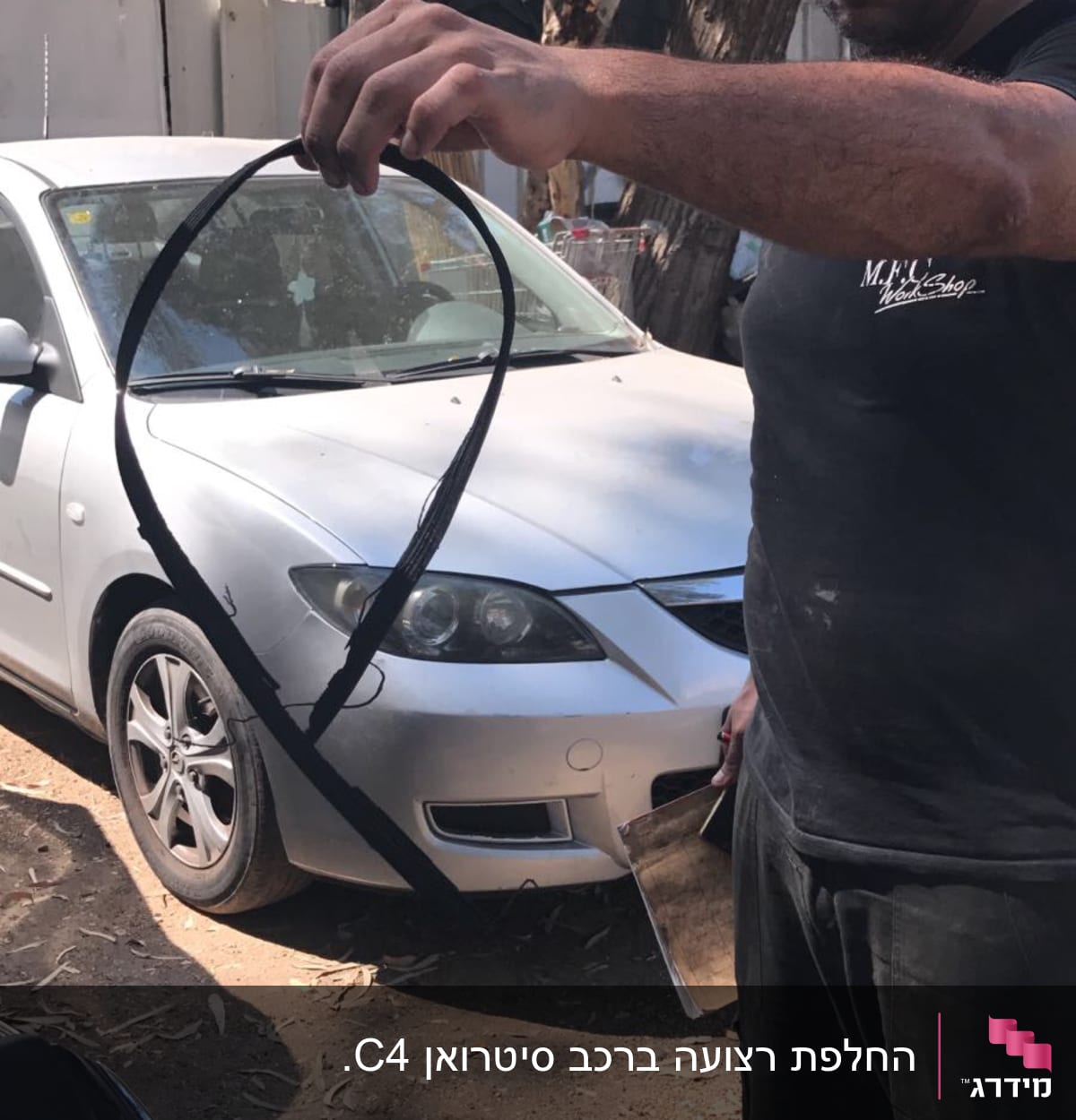 אדם מחזיק רצועת מנוע ליד רכב לבן